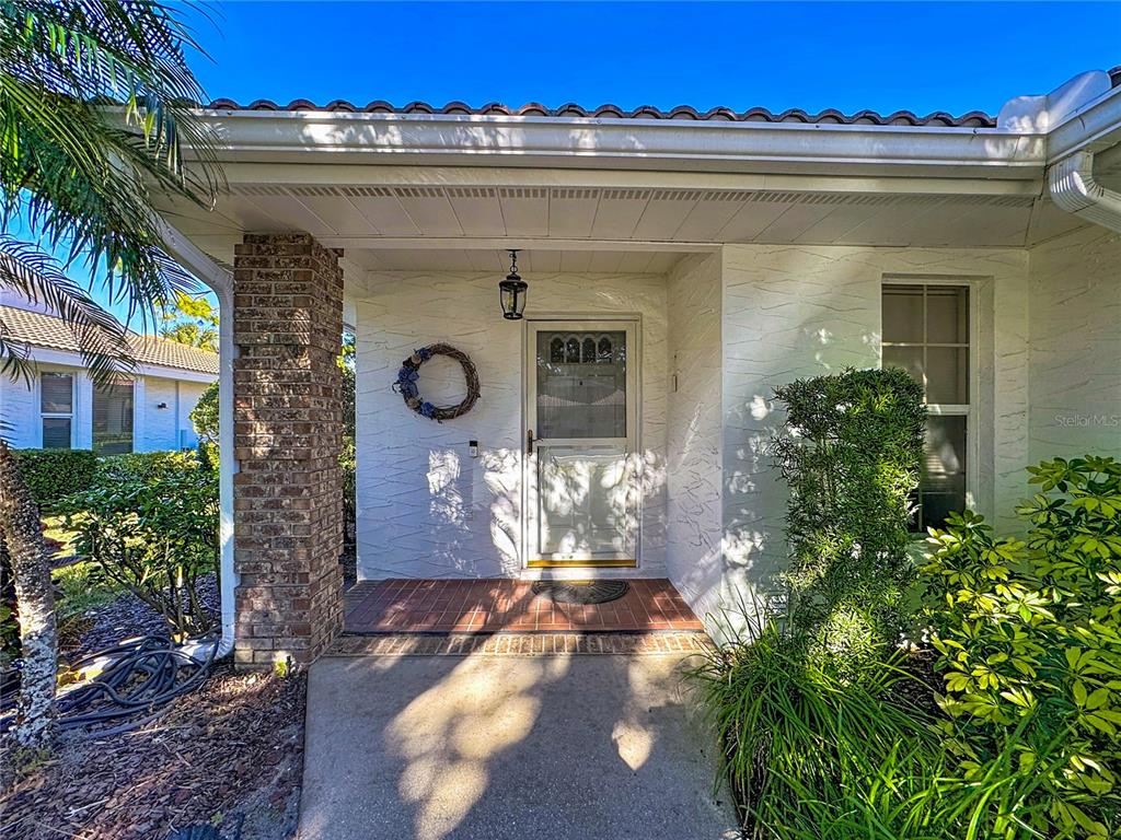 A white stucco house exterior features a brick column, a front door, and landscaping — 5611 GARDEN LAKES DRIVE, BRADENTON, FL