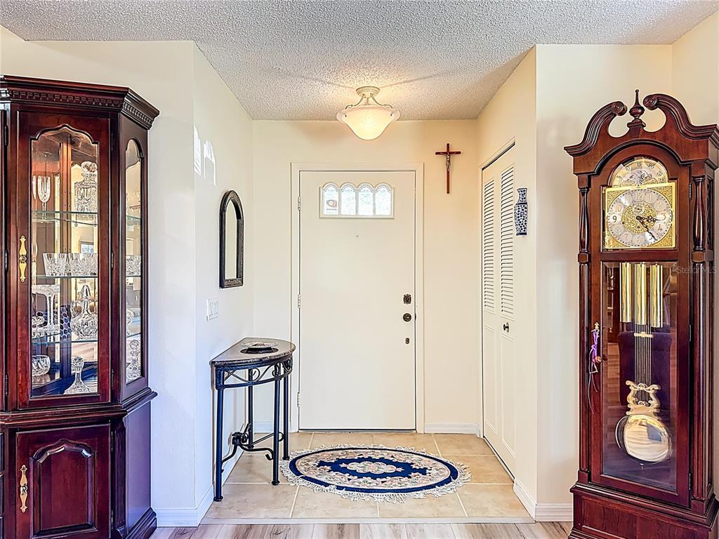 An entryway features a white front door, a grandfather clock, a curio cabinet, and tile flooring — 5611 GARDEN LAKES DRIVE, BRADENTON, FL