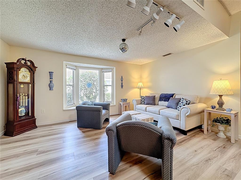 A living room features a grandfather clock, a bay window, and light wood-look flooring — 5611 GARDEN LAKES DRIVE, BRADENTON, FL