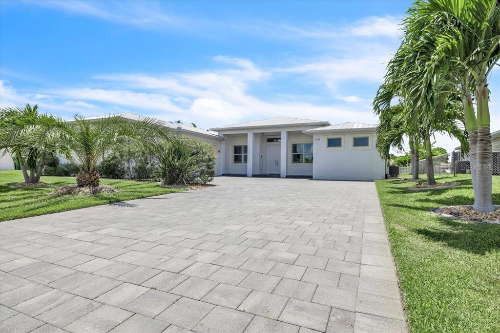 A single-story house with a paved driveway, white exterior, and palm trees under a blue sky — 2918 SE 10TH PLACE, CAPE CORAL, FL