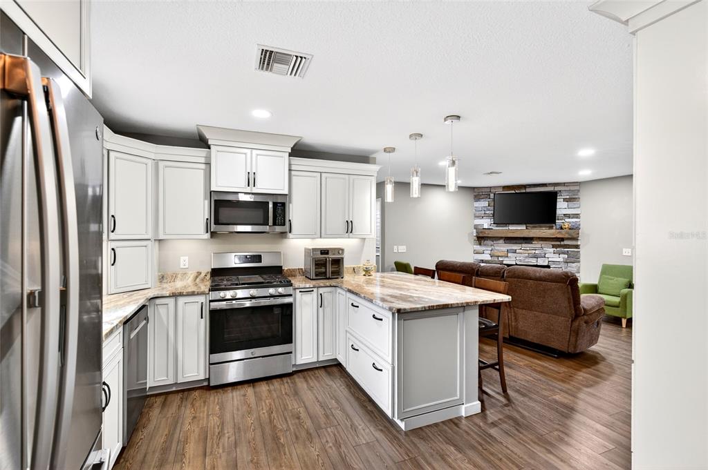 A kitchen with white cabinets and stone countertops opens into a living room with fireplace — 14271 NE 47TH AVENUE, ANTHONY, FL