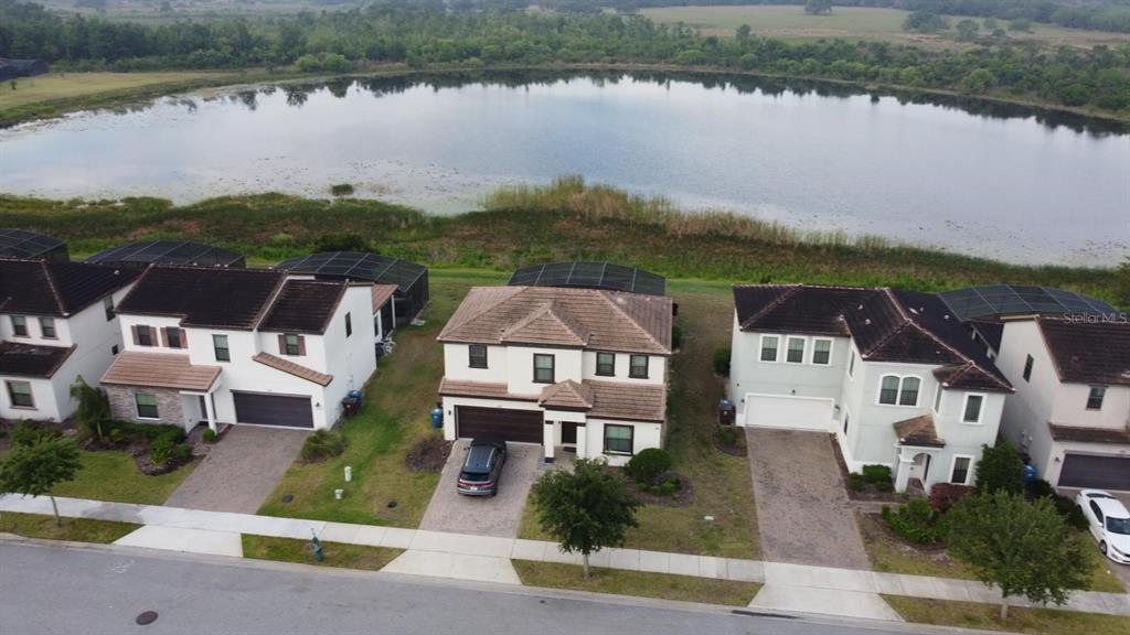 An aerial view shows three suburban houses with screened-in lanais facing a large lake — 179 MITCHELLS MANOR, HAINES CITY, FL
