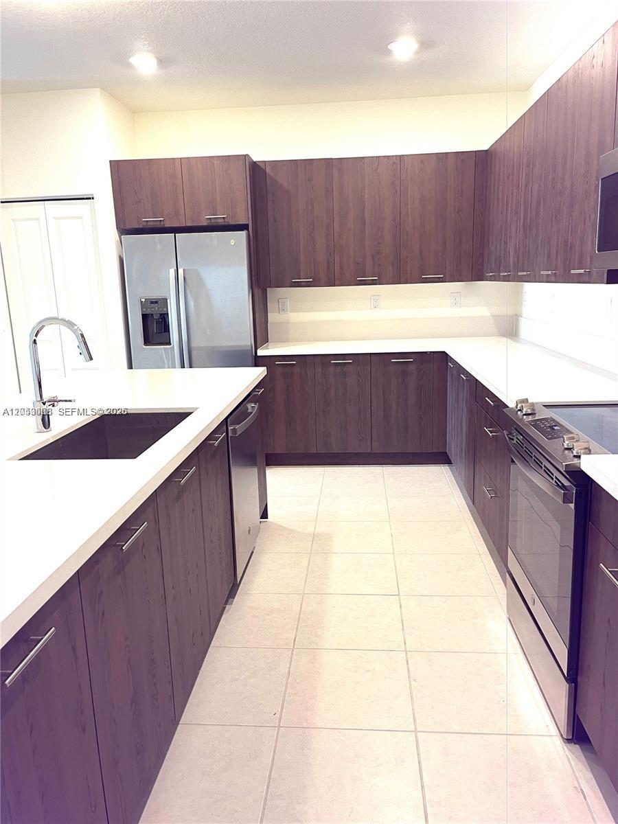A modern kitchen features dark wood cabinets, stainless steel appliances, and white countertops — 4576 NW 83rd Path, Doral FL 33166, DORAL, FL