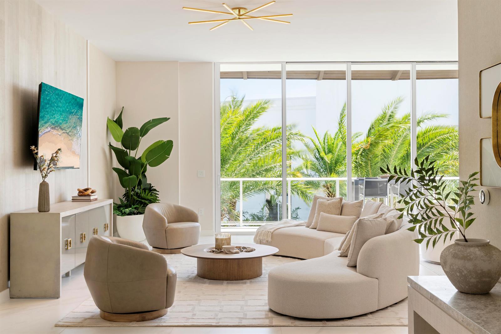 A bright living room features a curved sofa, two armchairs, and floor-to-ceiling windows with palms — 220 SE Mizner Boulevard, Boca Raton FL 33432, BOCA RATON, FL