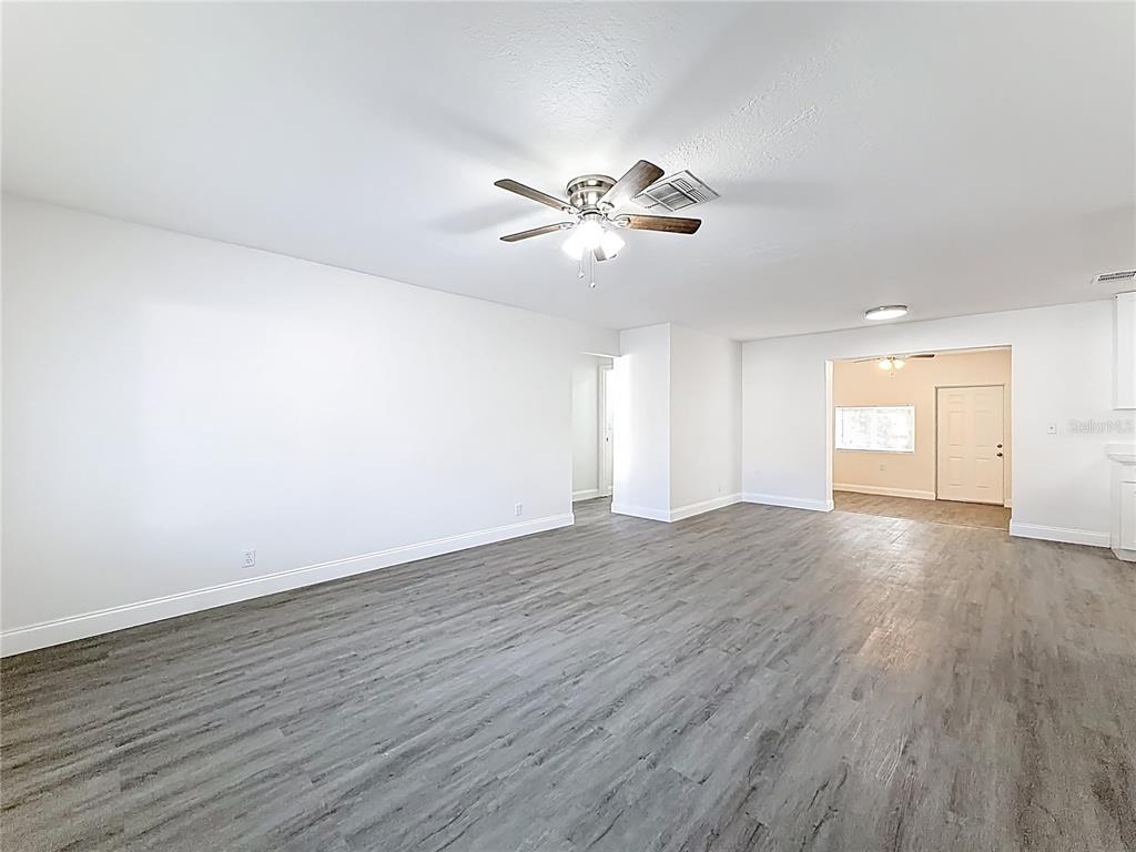 A spacious room with white walls, a ceiling fan, and gray wood-look flooring — 819 HELMSMAN WAY, PALM HARBOR, FL