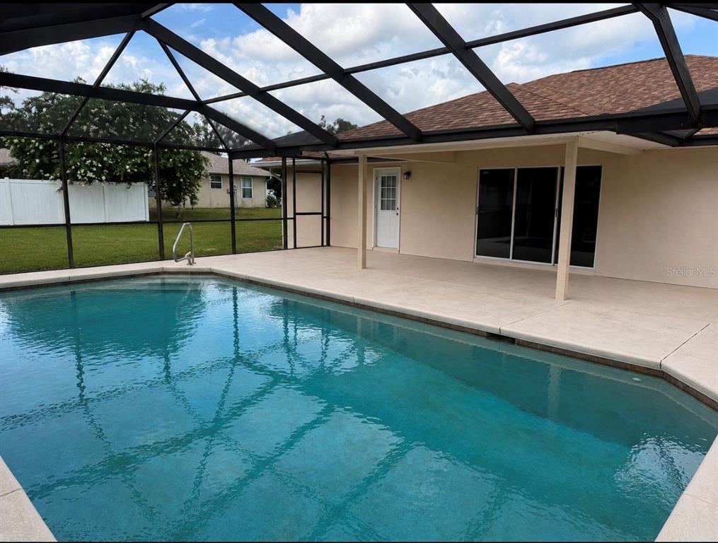 A backyard view of a house with a screened-in pool enclosure and palm trees — 4025 NE 14TH COURT, OCALA, FL