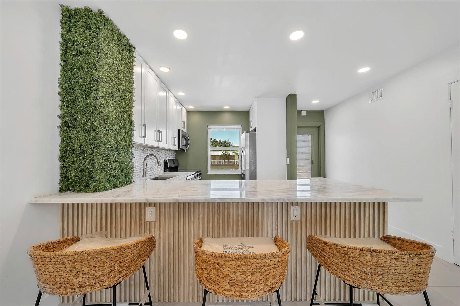 A kitchen features white cabinets, a marble-topped island with wood slats, and a vertical garden wall — 9818 Marina Boulevard # 1225, Boca Raton FL 33428, BOCA RATON, FL