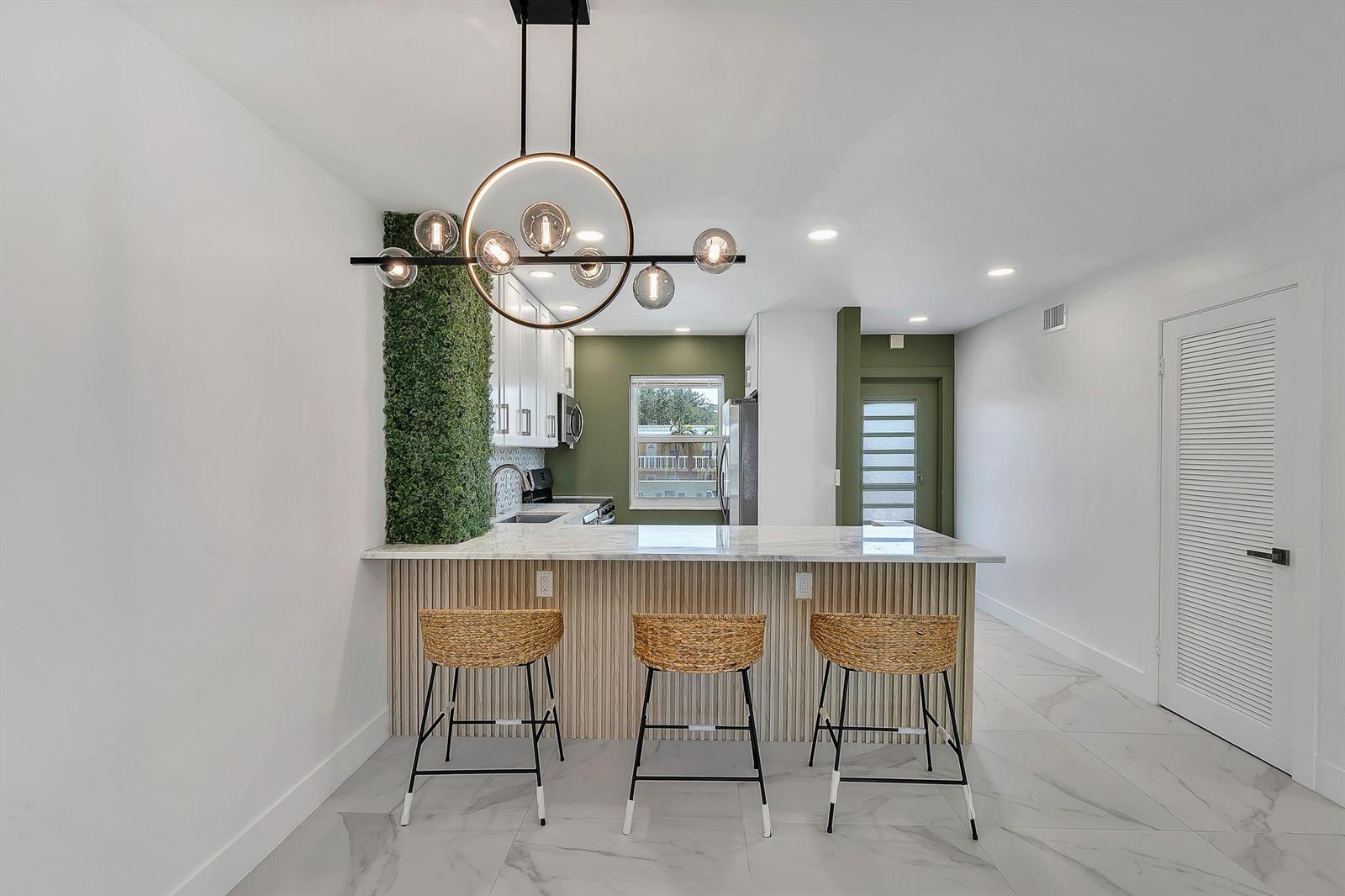 A kitchen features a marble-topped breakfast bar with three woven stools and green accent walls — 9818 Marina Boulevard # 1225, Boca Raton FL 33428, BOCA RATON, FL