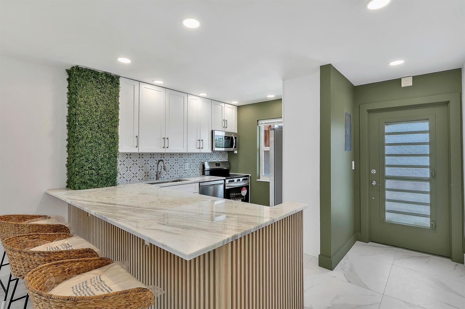 A kitchen features a marble-topped island, white cabinets, a green accent wall, and a door — 9818 Marina Boulevard # 1225, Boca Raton FL 33428, BOCA RATON, FL