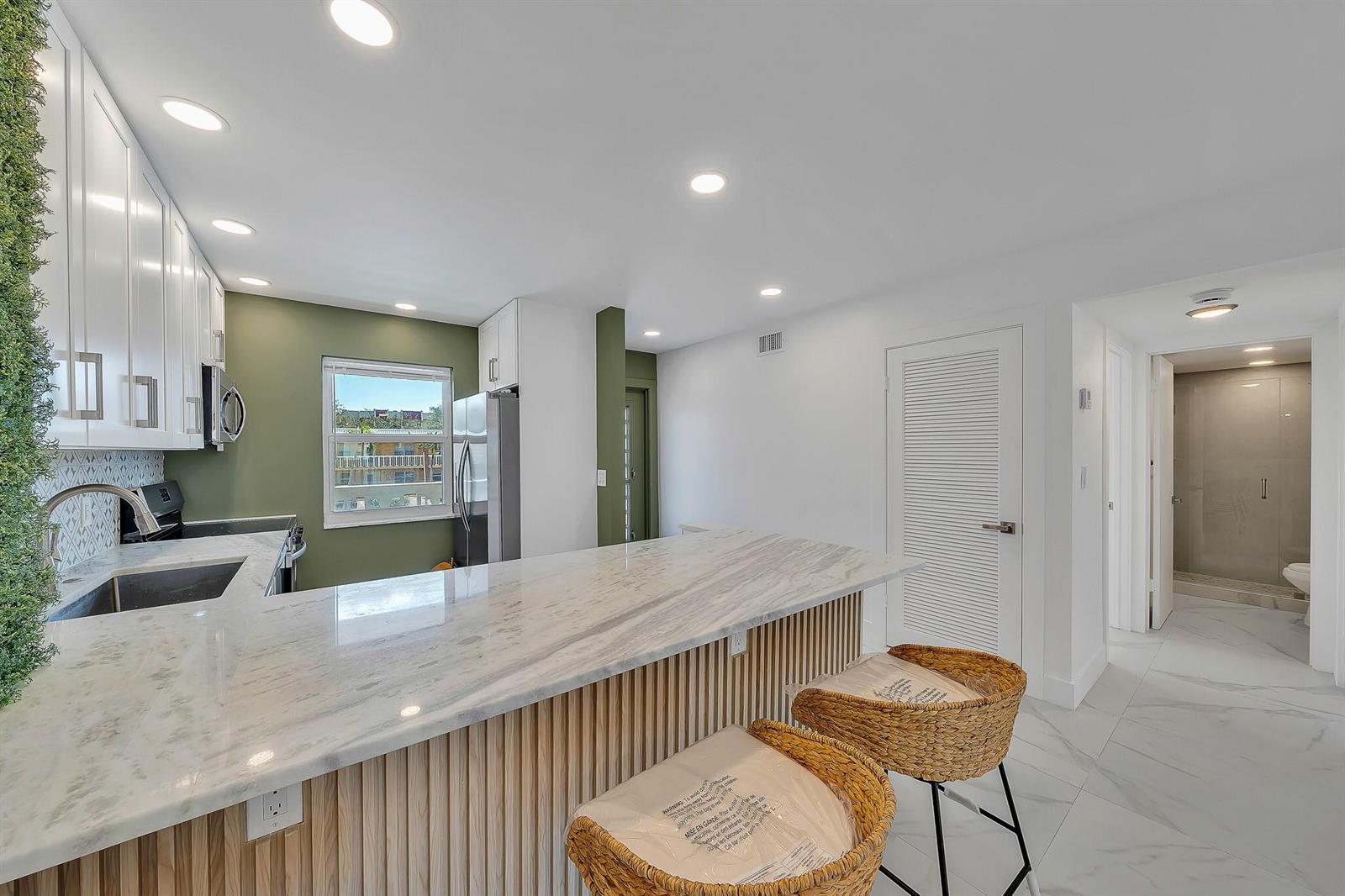 A kitchen features white cabinets, a marble countertop island with wood paneling, and green walls — 9818 Marina Boulevard # 1225, Boca Raton FL 33428, BOCA RATON, FL