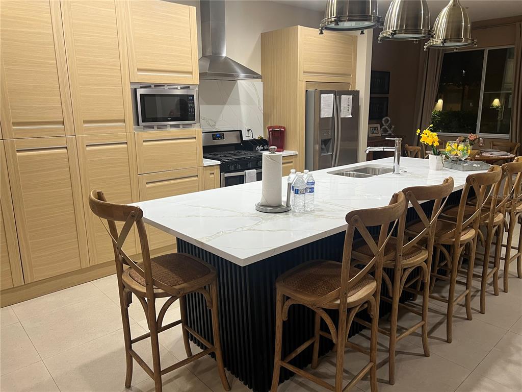 A modern kitchen features light wood cabinets, a white quartz island, and black slatted base — 3120 BRASILIA AVENUE, KISSIMMEE, FL