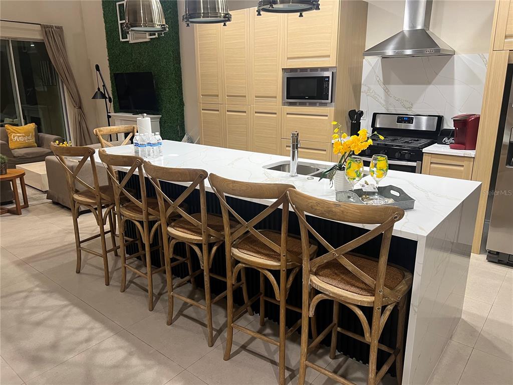 A kitchen island with four wooden chairs sits in front of light-colored cabinets and appliances — 3120 BRASILIA AVENUE, KISSIMMEE, FL