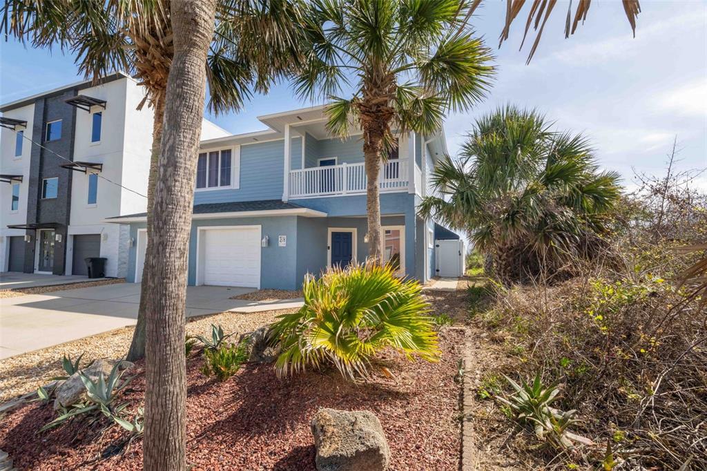 A two-story blue house with a white garage and a balcony stands near palm trees — 2708 S OCEAN SHORE BOULEVARD, FLAGLER BEACH, FL