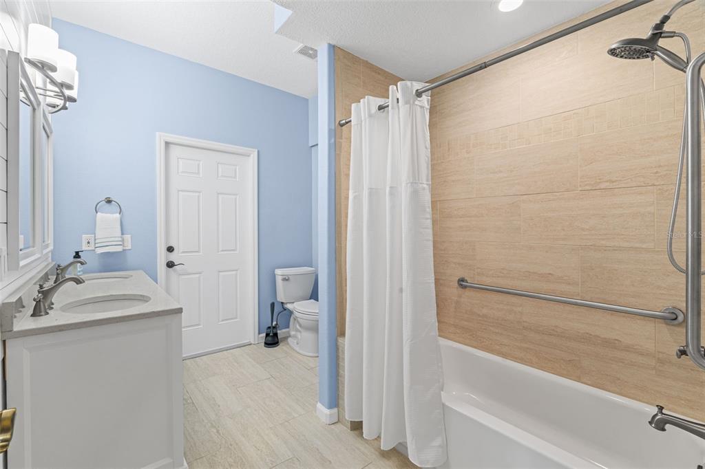 A bathroom features a double vanity, a toilet, and a shower-tub combo with tiled walls — 2708 S OCEAN SHORE BOULEVARD, FLAGLER BEACH, FL