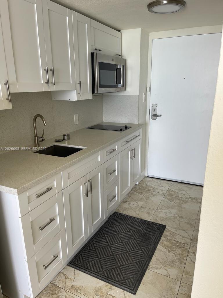 A small kitchen features white cabinets, light countertops, a built-in microwave, and tiled flooring — SUNNY ISLES BEACH, FL