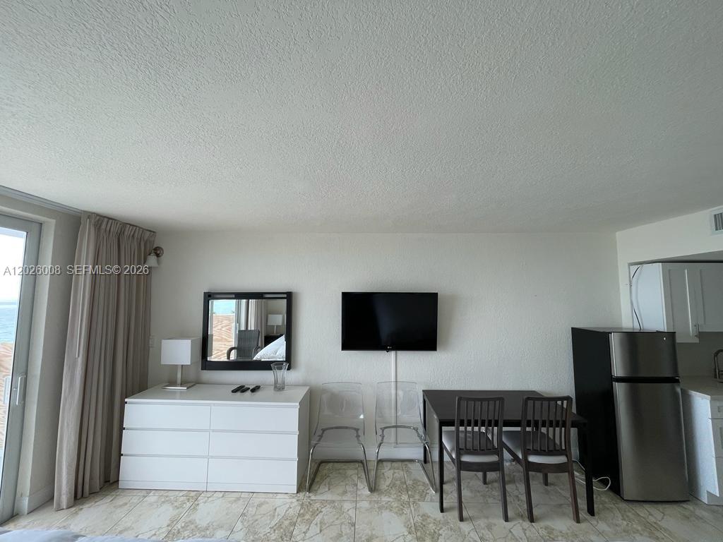 A room features a white dresser, a wall-mounted television, and a dining table with chairs — SUNNY ISLES BEACH, FL