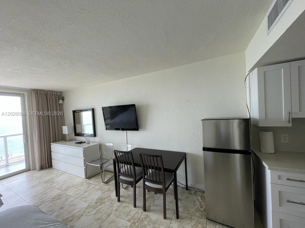 A studio apartment features a dining area, a television, and a stainless steel refrigerator — SUNNY ISLES BEACH, FL