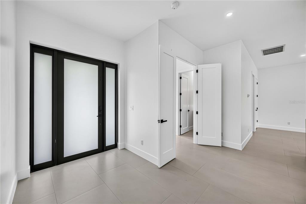 A modern entryway features light gray tile flooring, white walls, and a black-framed glass door — 18420 JEFFERSON AVENUE, PORT CHARLOTTE, FL