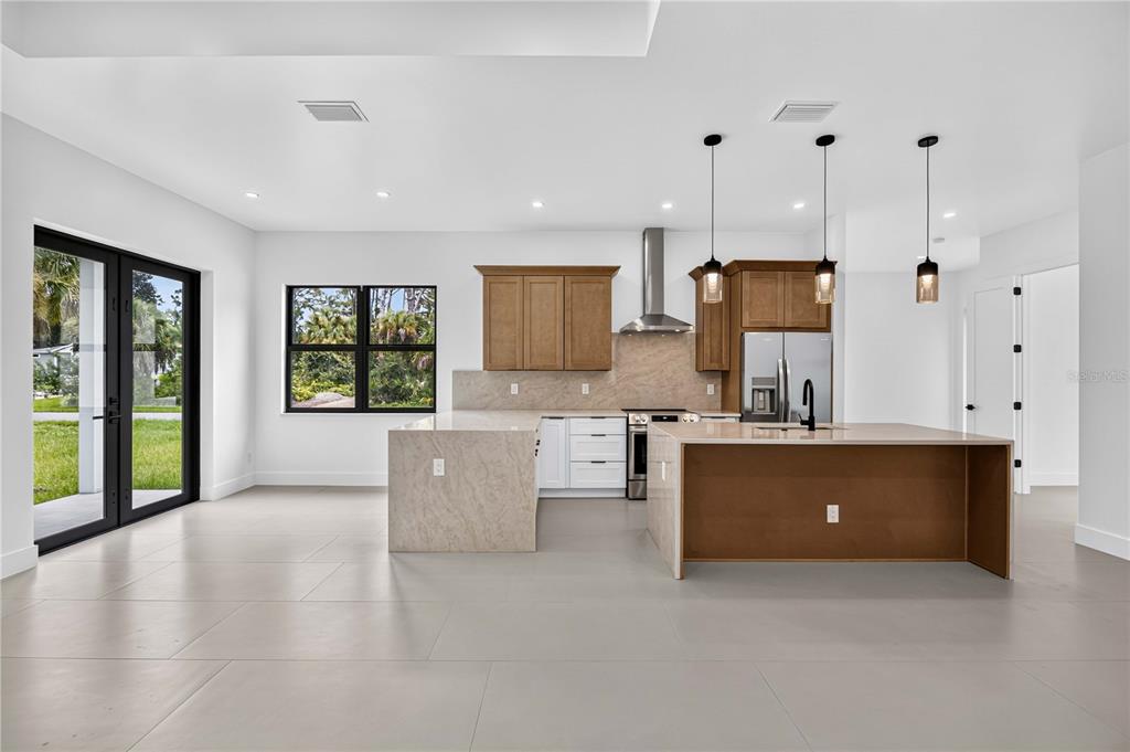 A modern kitchen features white walls, light tile floors, wood cabinets, and a large island — 18420 JEFFERSON AVENUE, PORT CHARLOTTE, FL