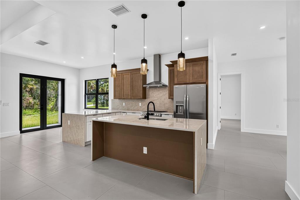 A modern kitchen features a large island, stainless steel appliances, and brown cabinetry — 18420 JEFFERSON AVENUE, PORT CHARLOTTE, FL