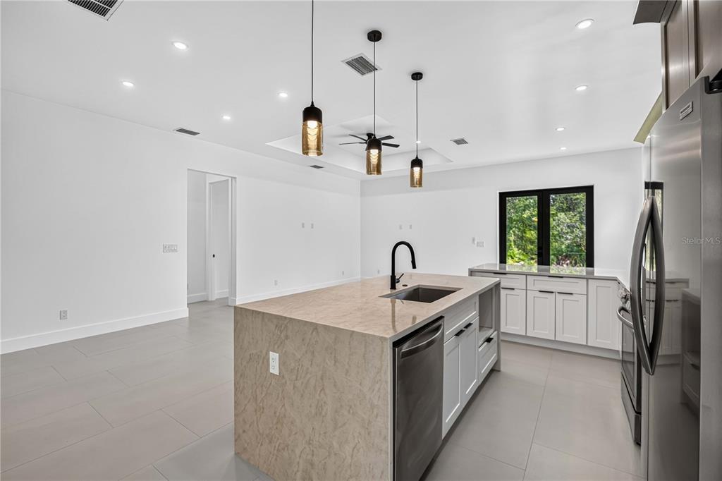 A modern kitchen features a stone-topped island, white cabinetry, stainless steel appliances, and pendant lighting — 18420 JEFFERSON AVENUE, PORT CHARLOTTE, FL