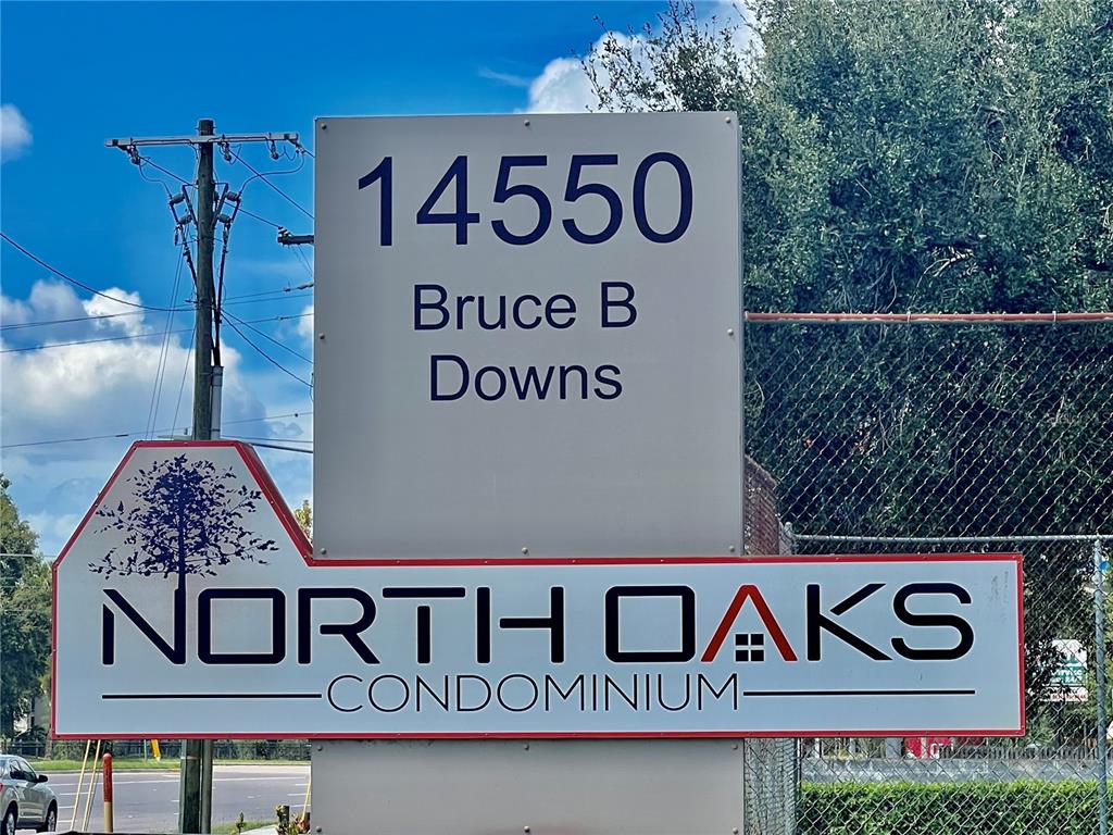 A sign for North Oaks Condominium stands outdoors near a utility pole and chain-link fence — 4025 ANGEL OAK COURT UNIT 203, TAMPA, FL