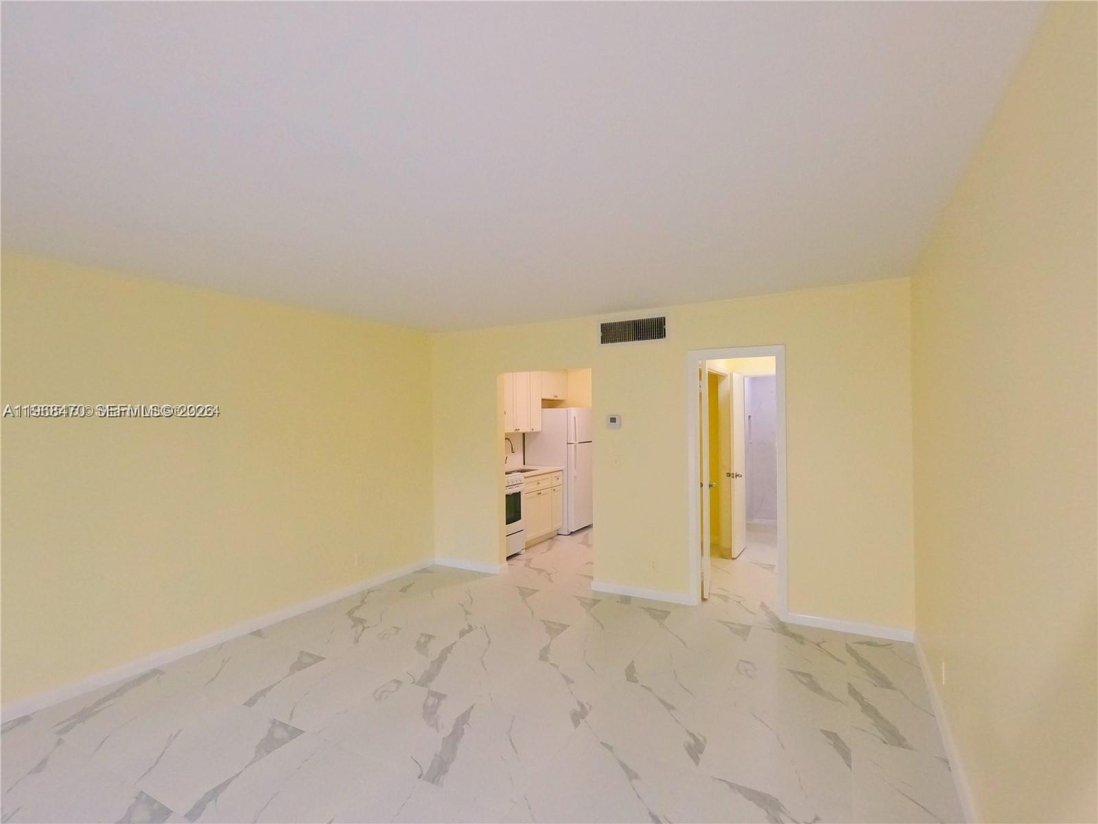 A living area with light yellow walls and white marble-patterned tile flooring leads to a kitchen — 644 NW 13th St # 0120, Boca Raton FL 33486, BOCA RATON, FL