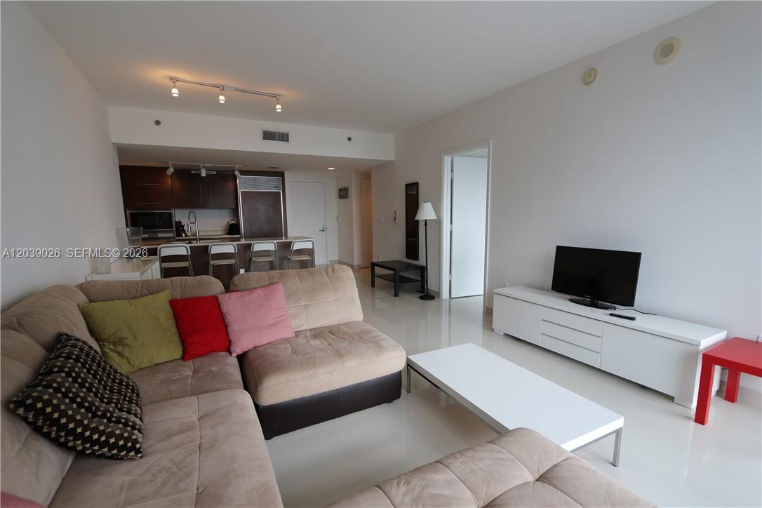 A living room features a beige sectional sofa, white media console, and an open kitchen — 465 Brickell Ave # 4706, Miami FL 33131, MIAMI, FL