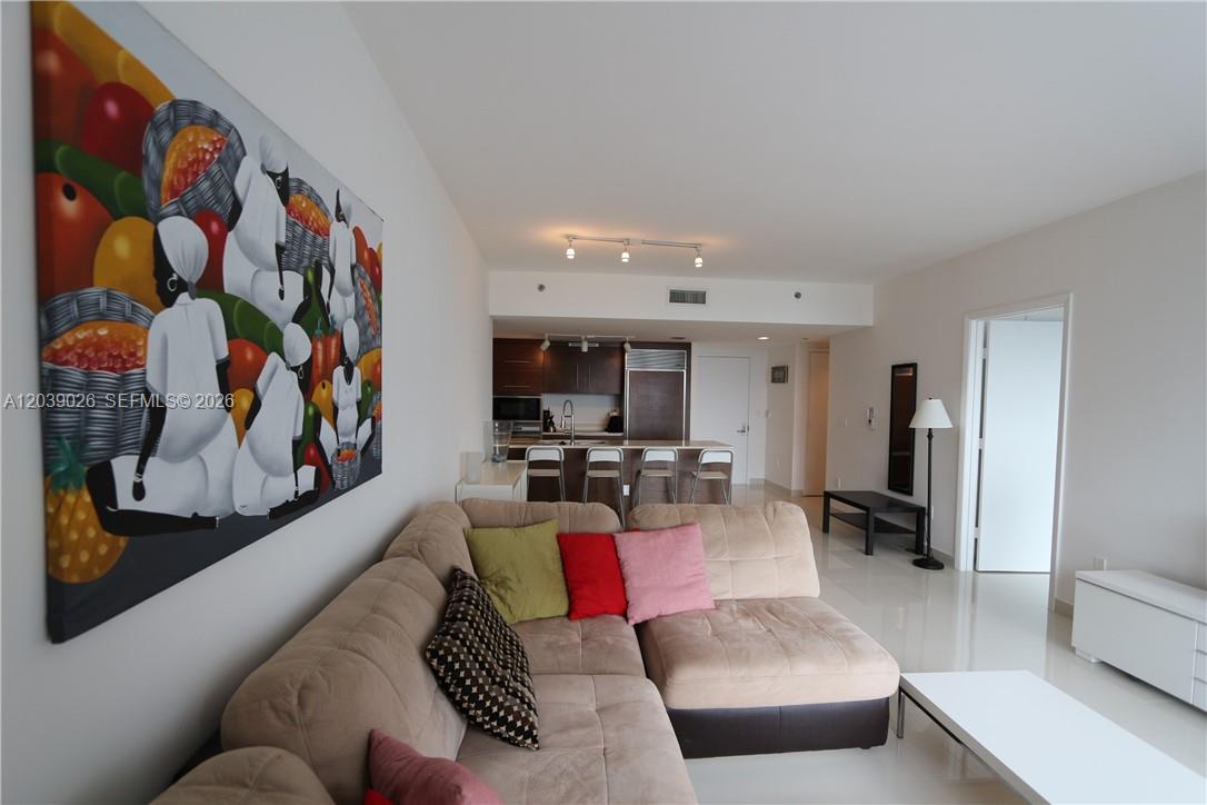 A living room with a beige sectional sofa, colorful pillows, and an open kitchen — 465 Brickell Ave # 4706, Miami FL 33131, MIAMI, FL