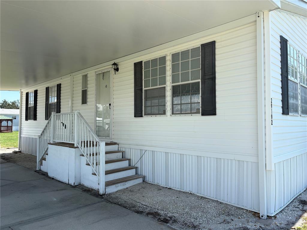 A white mobile home exterior features a covered carport, a front door, and wooden stairs — 29192 CRAWFORD AVENUE, PUNTA GORDA, FL