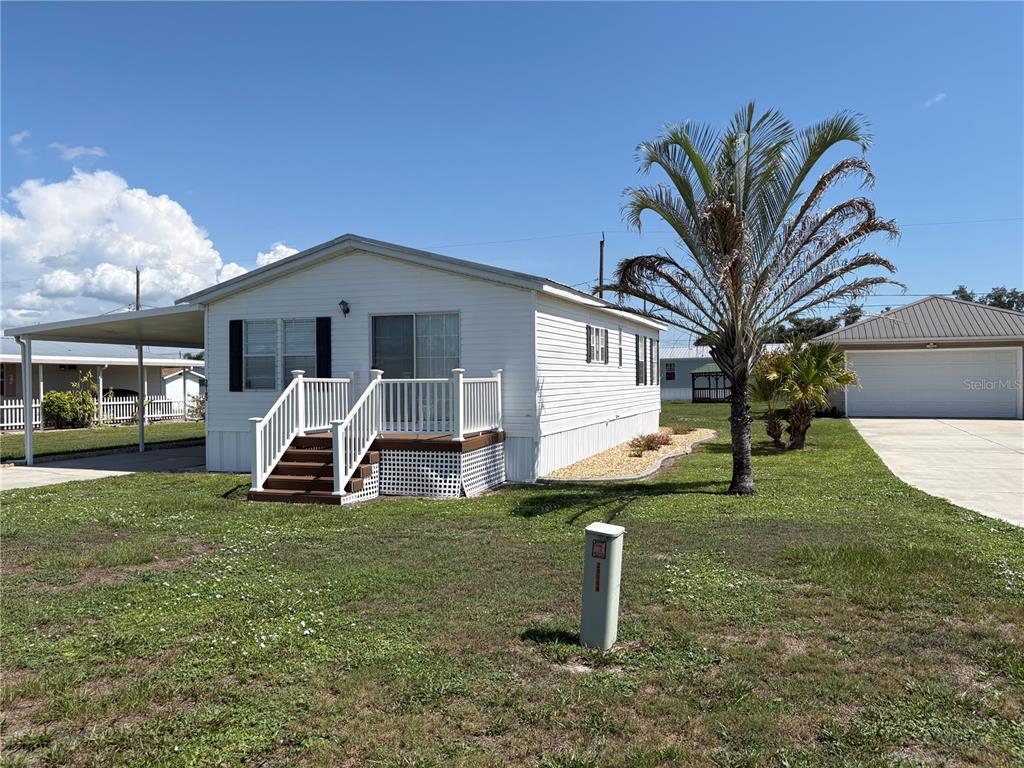 A white mobile home features a wooden front deck, a carport, and a palm tree — 29192 CRAWFORD AVENUE, PUNTA GORDA, FL