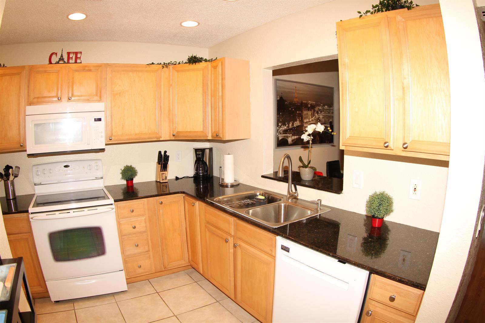 A kitchen features light wood cabinets, black granite countertops, white appliances, and a pass-through window — 1308 White Pine Drive, Wellington FL 33414, WELLINGTON, FL
