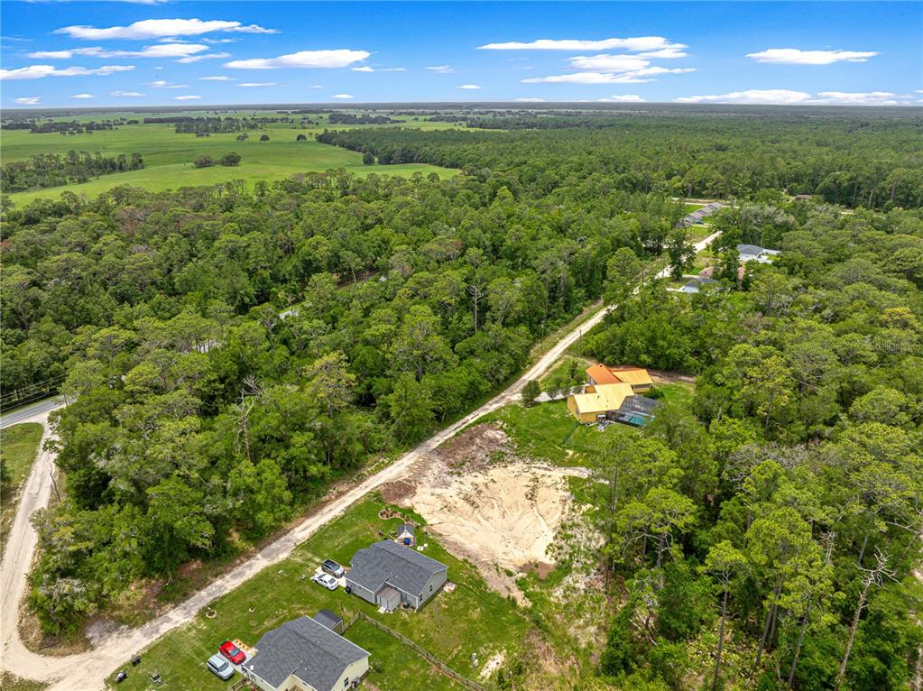 An aerial view shows several houses surrounded by dense forest and open grassy fields — SW 41ST STREET ROAD, OCALA, FL