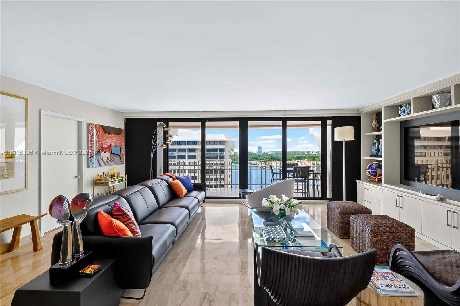 A modern living room features a leather sofa, glass coffee table, and balcony with water views — 2 Grove Isle Dr # B1804, Coconut Grove FL 33133, COCONUT GROVE, FL
