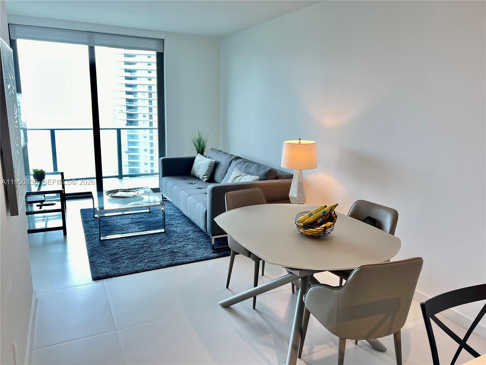 A modern living and dining area features a gray sofa, glass coffee table, and dining set — 501 NE 31st St # 2204, Miami FL 33137, MIAMI, FL