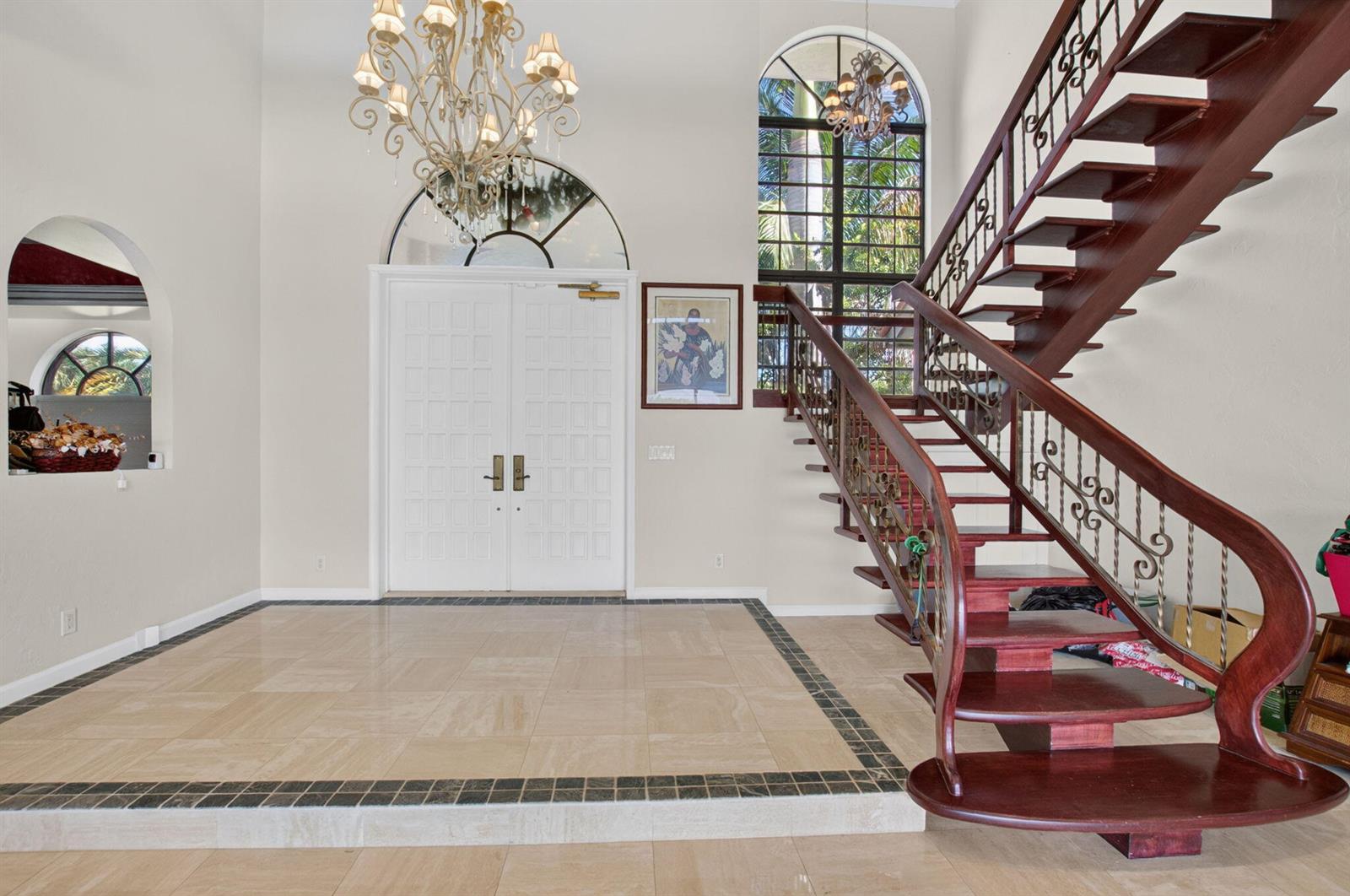 A grand foyer features a tiled floor, a large chandelier, and a wooden staircase — 10792 El Caballo Court, Delray Beach FL 33446, DELRAY BEACH, FL