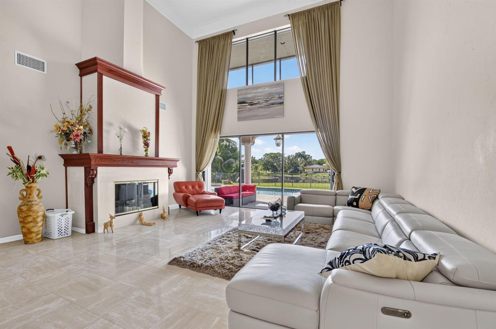 A high-ceilinged living room features a fireplace, large windows, tile floors, and a sectional sofa — 10792 El Caballo Court, Delray Beach FL 33446, DELRAY BEACH, FL