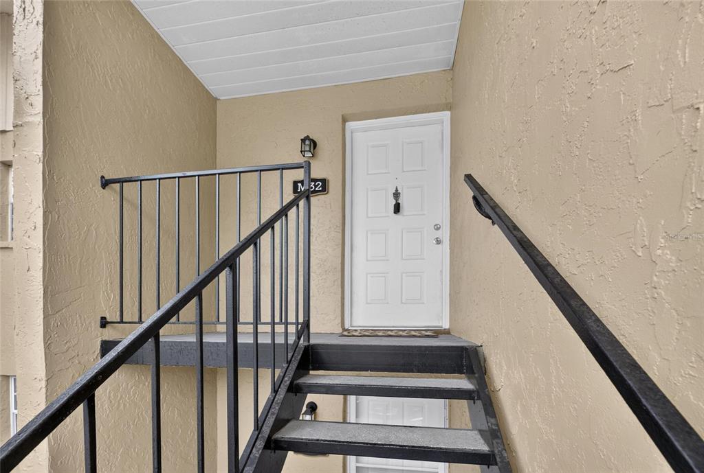 An exterior view of a white front door at the top of metal stairs — 3812 N OAK DRIVE UNIT M32, TAMPA, FL