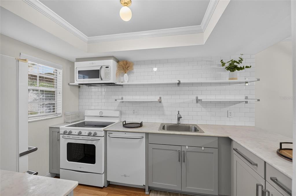A kitchen features gray cabinets, white subway tile backsplash, open shelving, and white appliances — 3812 N OAK DRIVE UNIT M32, TAMPA, FL