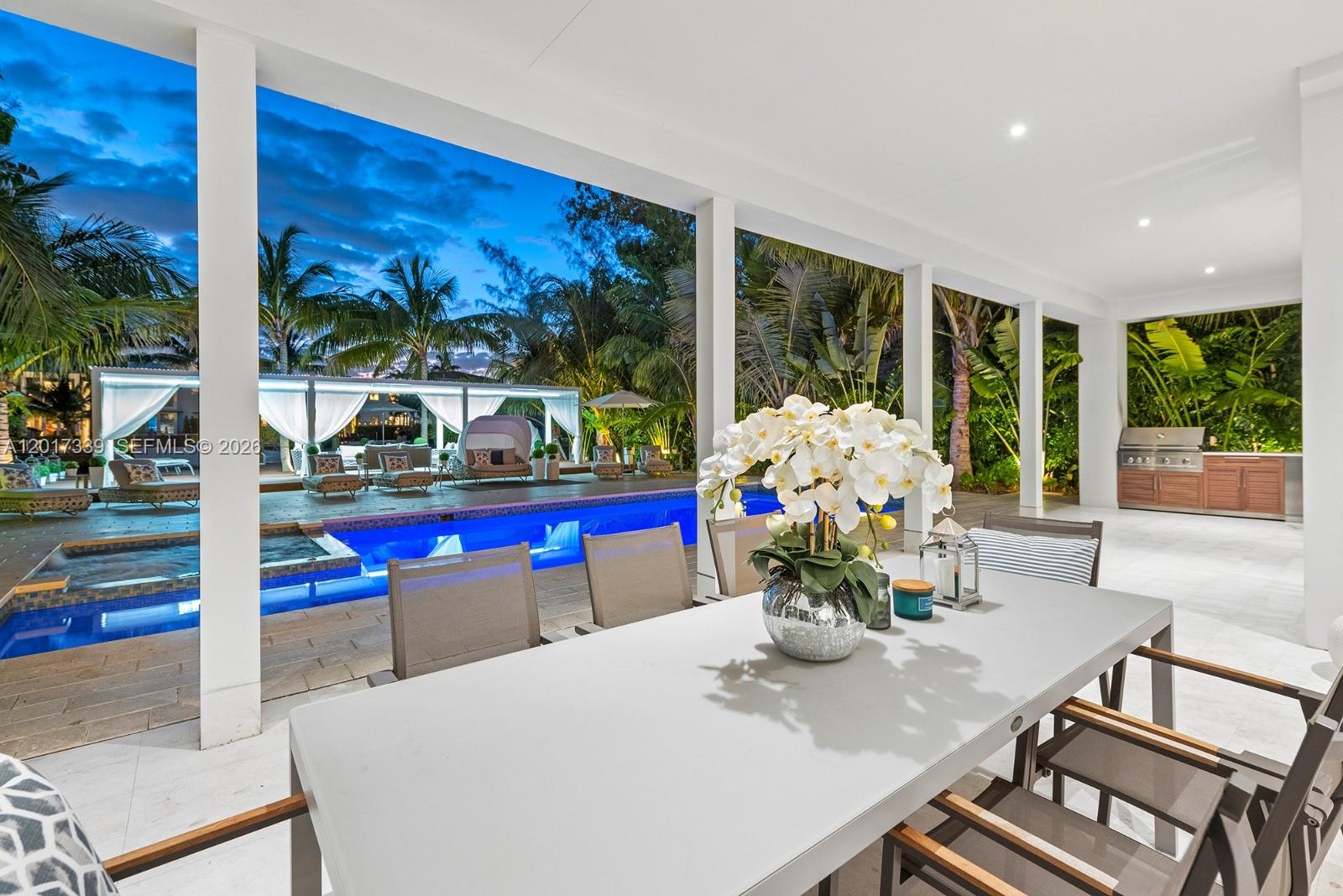 A covered outdoor dining area overlooks a swimming pool and a landscaped backyard at dusk — 3734 Chase Ave, Miami Beach FL 33140, MIAMI BEACH, FL