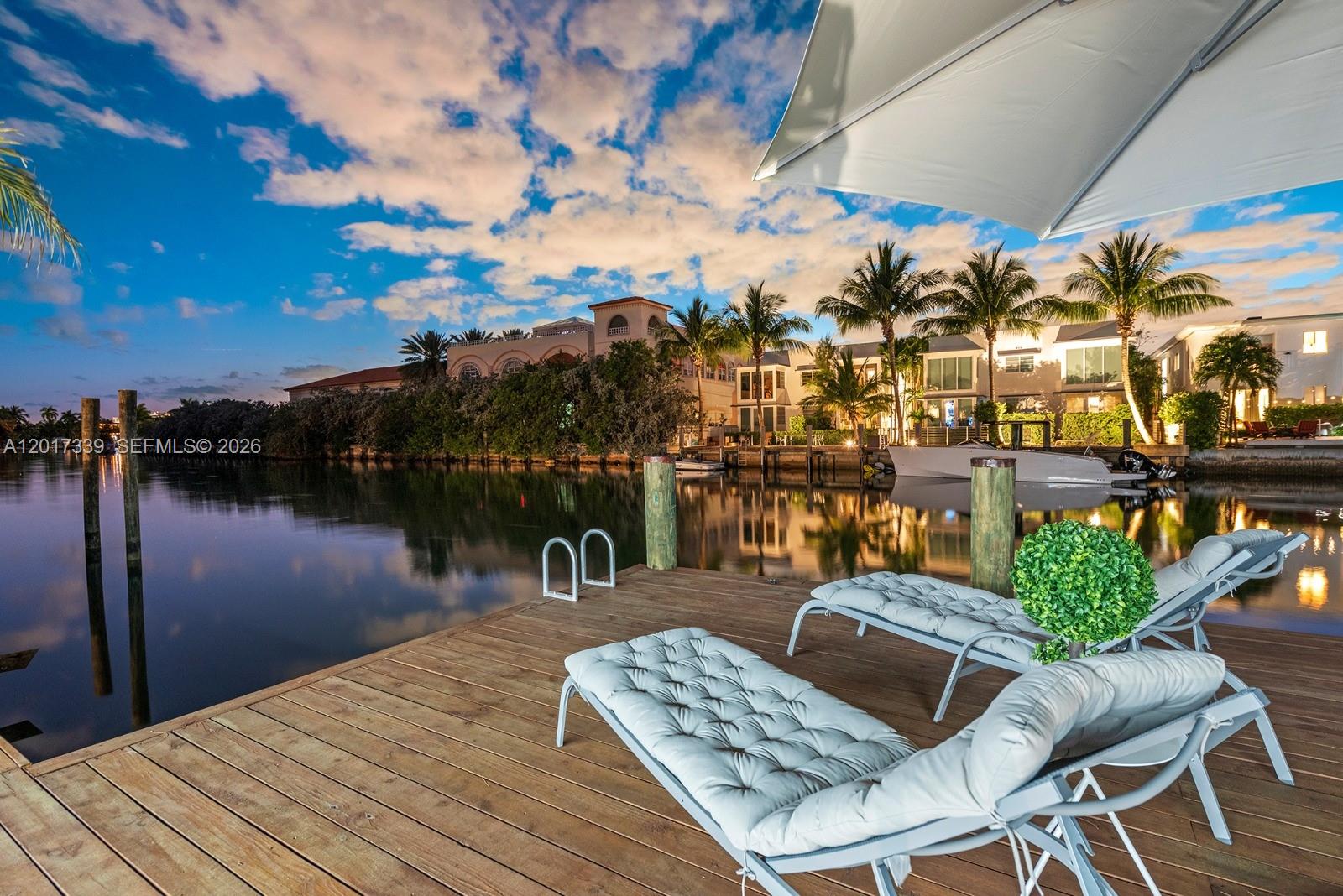 A wooden dock features two lounge chairs overlooking a canal with houses and palm trees — 3734 Chase Ave, Miami Beach FL 33140, MIAMI BEACH, FL