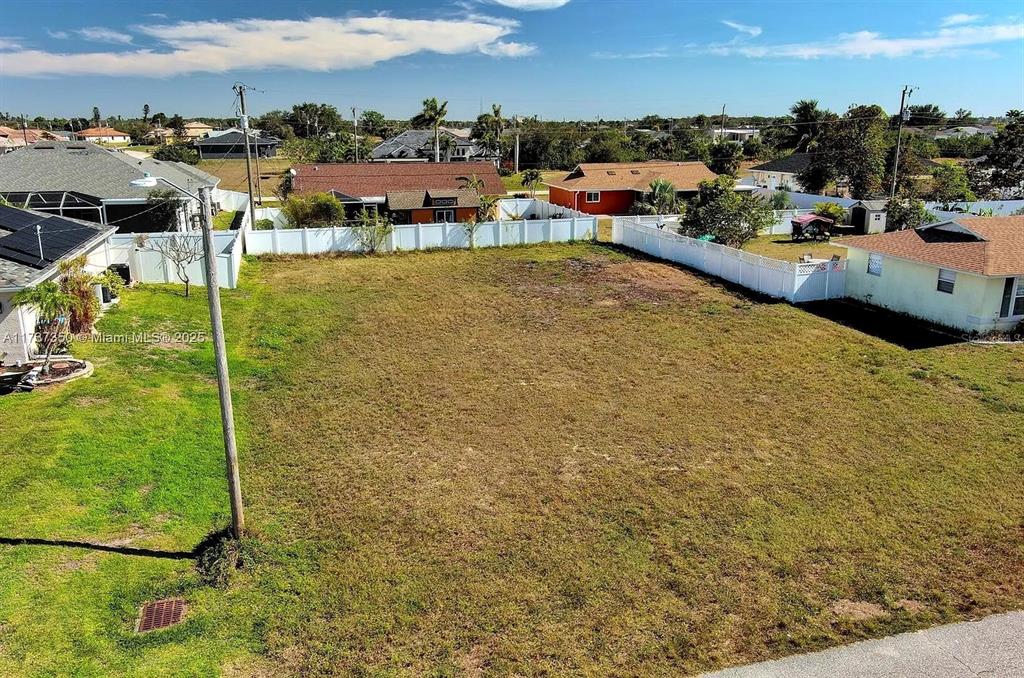 An elevated view shows a vacant, grassy residential lot enclosed by white vinyl fencing — 2013 NE 18TH AVENUE, CAPE CORAL, FL