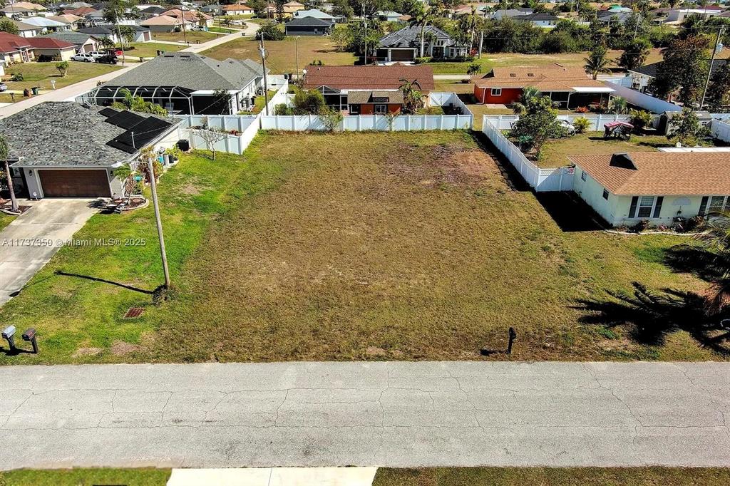 An aerial view shows a vacant, grassy residential lot situated between two existing houses — 2013 NE 18TH AVENUE, CAPE CORAL, FL