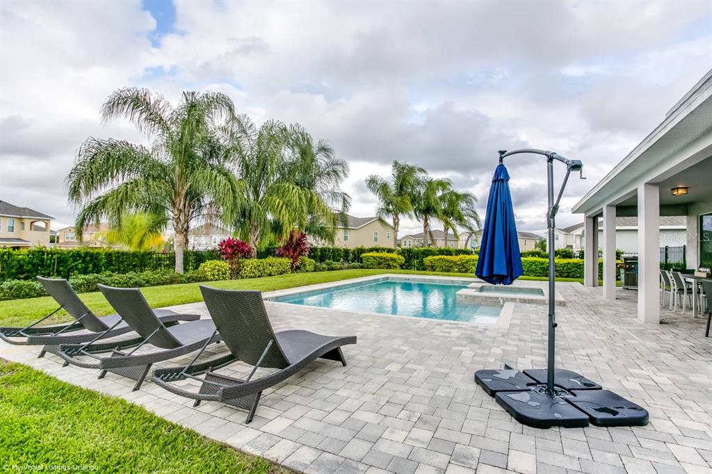 A backyard features a swimming pool, lounge chairs on a paver patio, and palm trees — 7736 GRABEN STREET, KISSIMMEE, FL