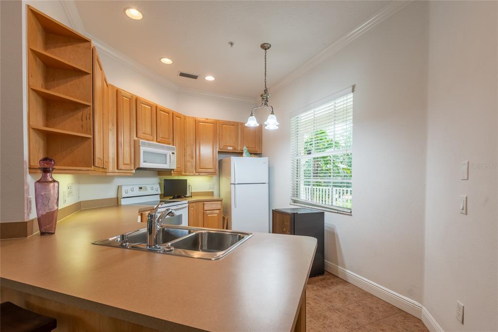 A kitchen features light wood cabinets, a laminate countertop, a double sink, and white appliances — 6815 DALI AVENUE UNIT 205, LAND O LAKES, FL