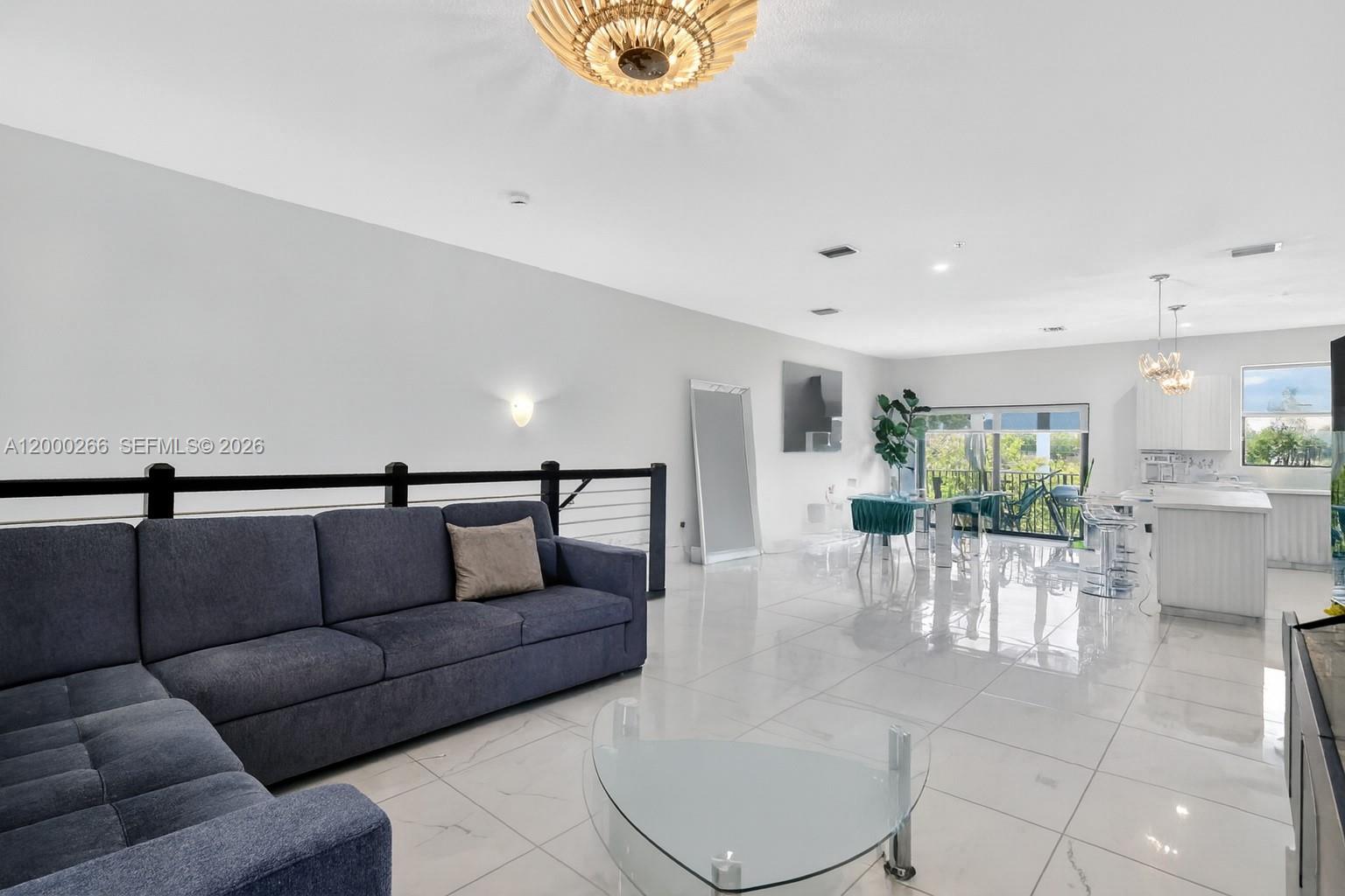 A bright, open-concept living area features a blue sectional sofa, tile flooring, and a kitchen — 10467 NW 82nd St # 11, Doral FL 33178, DORAL, FL