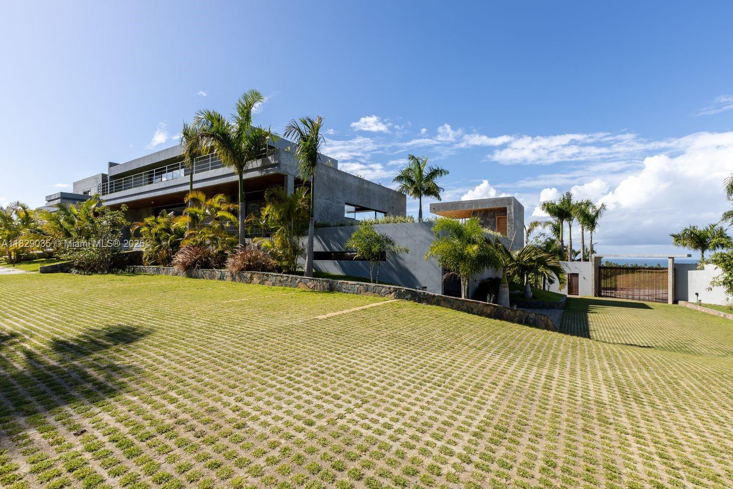 A modern concrete house with a large grass-paver driveway and palm trees under a blue sky — 000 8G99+hr Las Terrenas, Dominican Republic, FL 32000, FL