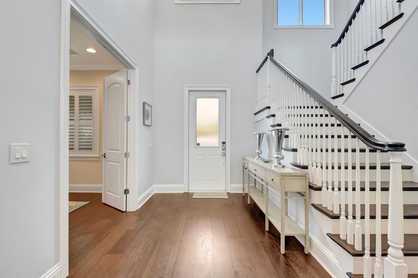 A bright foyer features hardwood floors, a staircase with dark railings, and a console table — 1507 Pine Lane, Delray Beach FL 33444, DELRAY BEACH, FL