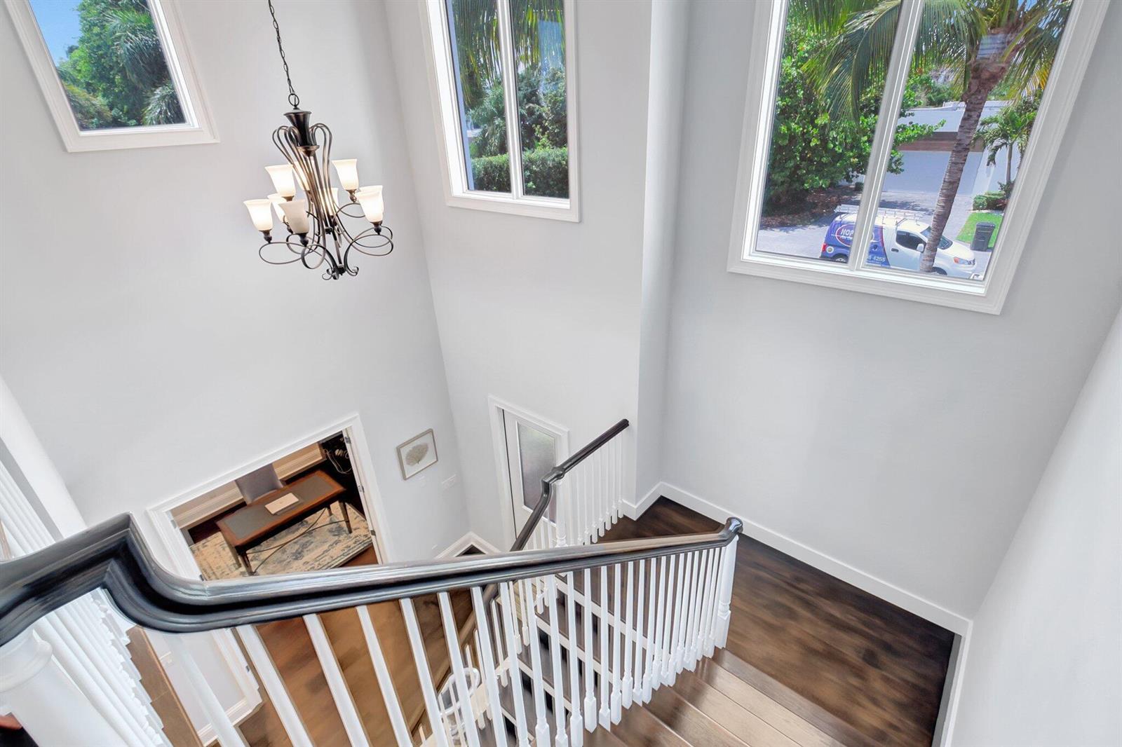A high-angle view of a staircase with dark wood treads, white railings, and a chandelier — 1507 Pine Lane, Delray Beach FL 33444, DELRAY BEACH, FL