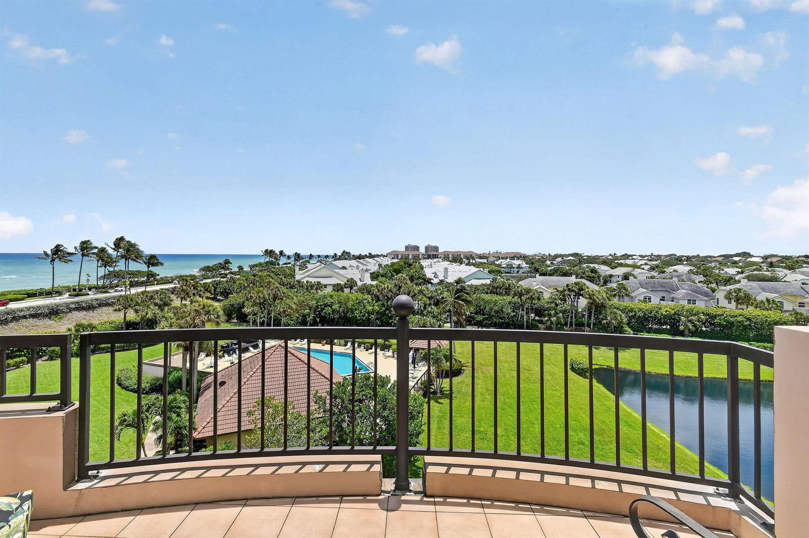 A balcony with a metal railing overlooks a swimming pool, green lawn, and the ocean — 101 Ocean Bluffs Boulevard # 504, Jupiter FL 33477, JUPITER, FL